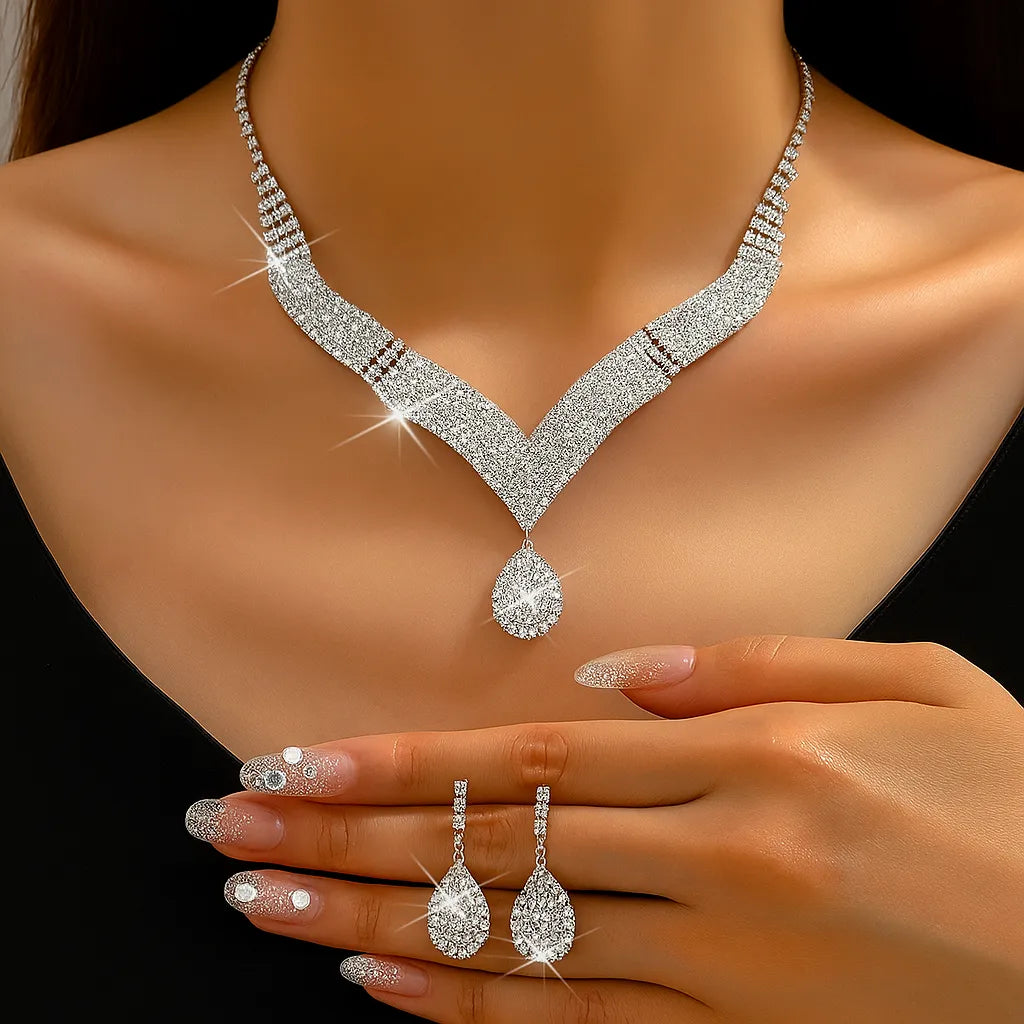 Conjunto de joias femininas ELIORA com colar e brincos de strass prateado formato gota sobre fundo azul, acessório elegante para festas e casamentos.